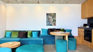 Een moderne zithoek met een blauwe bank, een ronde houten tafel en teal poufs.