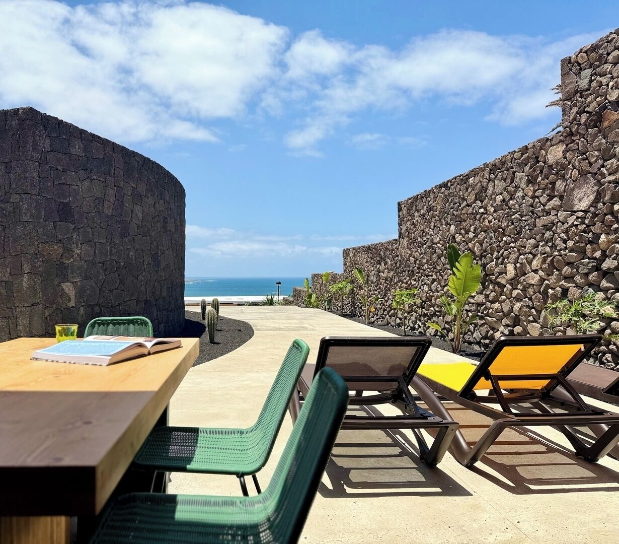 An outdoor seating area with a table and chairs, a stone wall, and a view of the ocean.