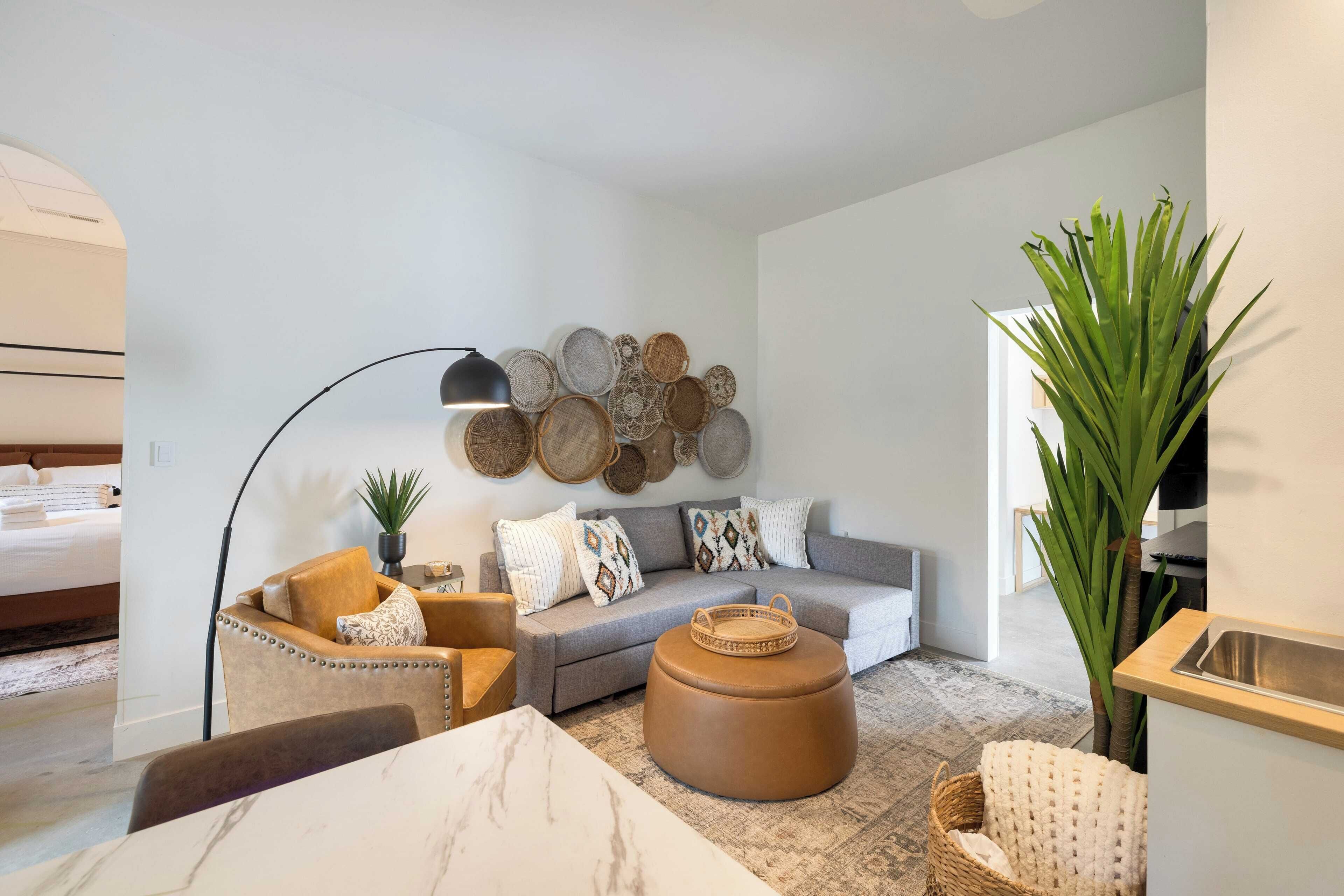 A modern living room with a sofa, armchair, ottoman, and a wall decorated with circular woven items.