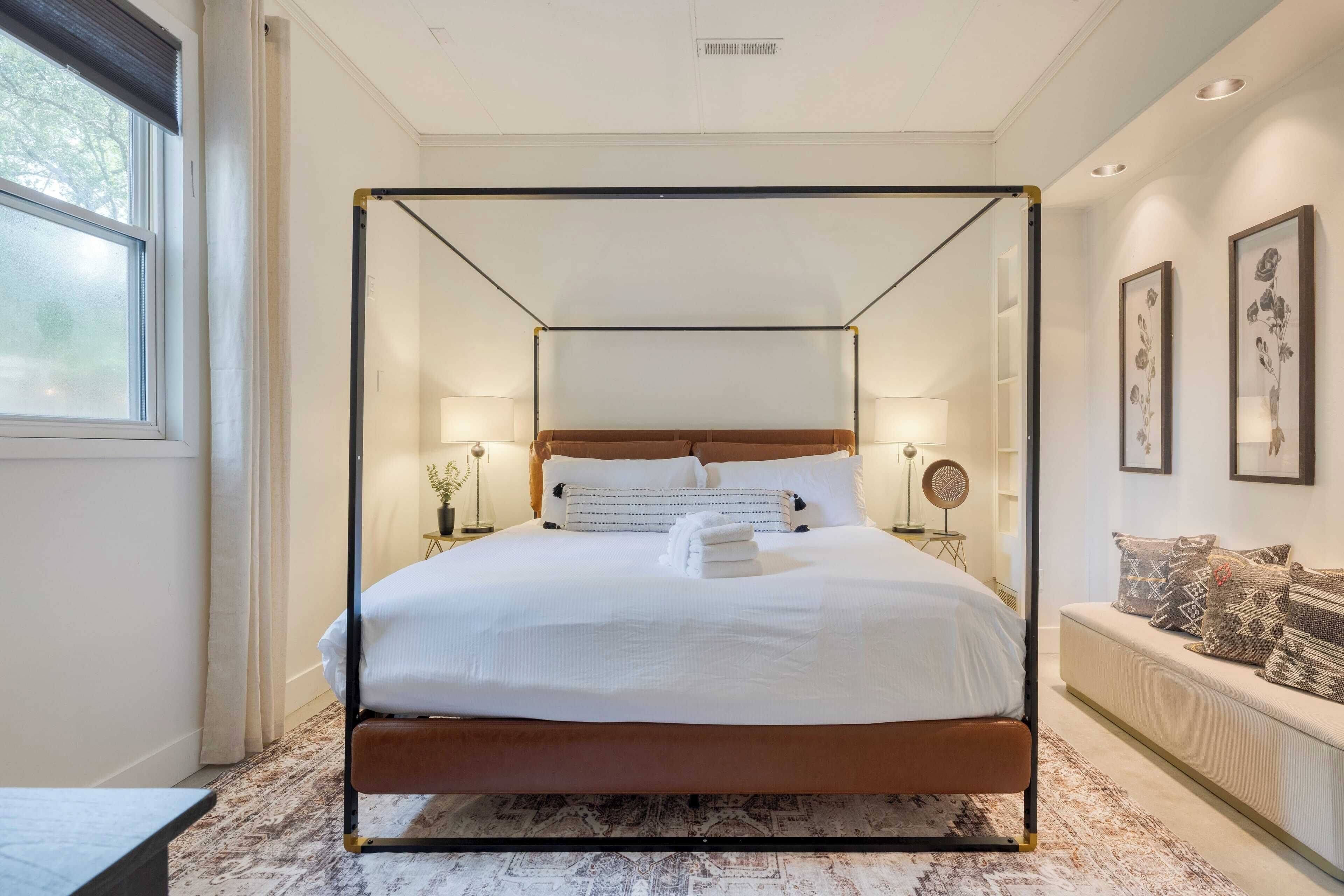 A four-poster bed with white linens, a wooden headboard, and a bedside table with a lamp.