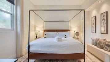 A four-poster bed with white linens, a wooden headboard, and a bedside table with a lamp.