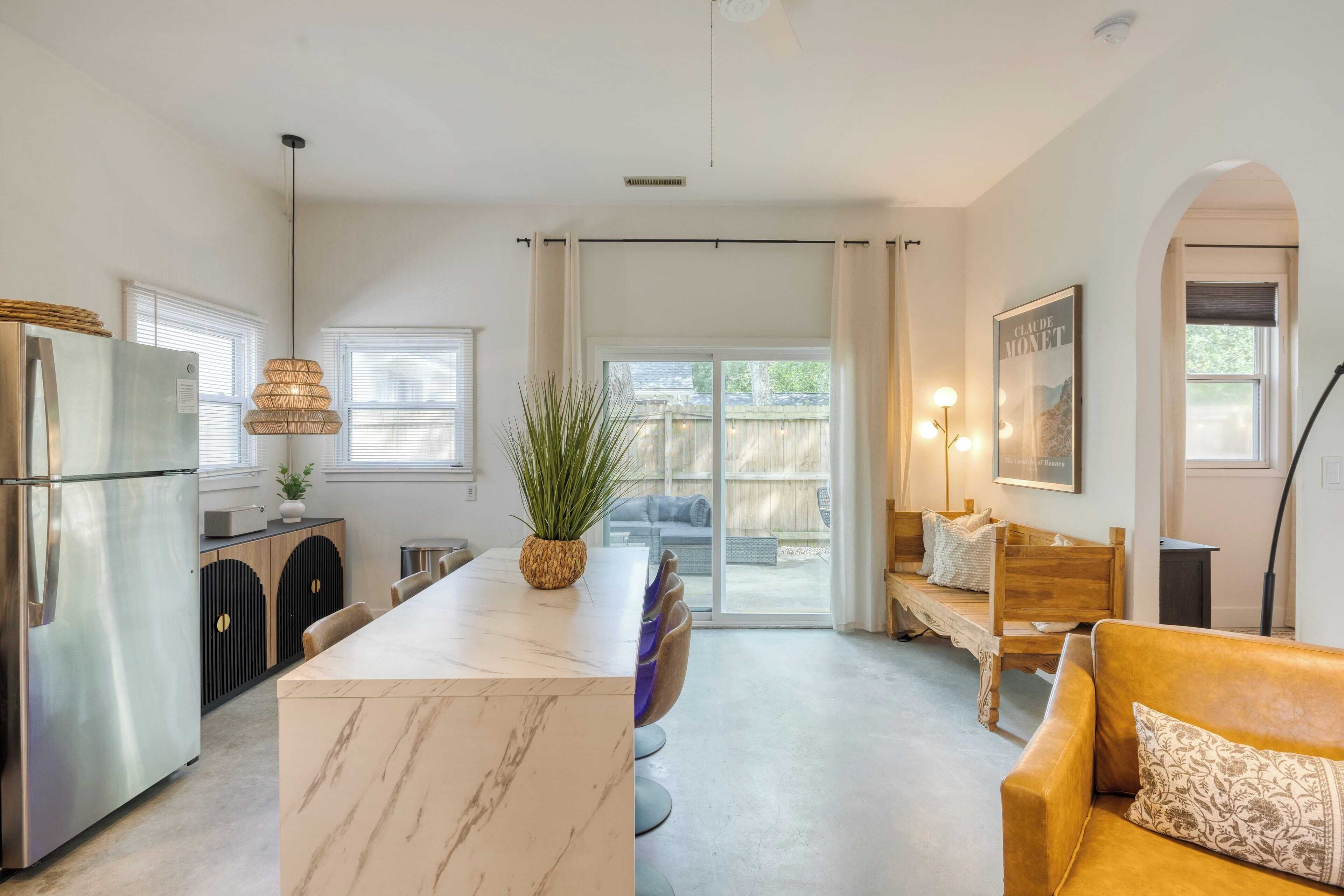 A modern kitchen with a marble island, stainless steel refrigerator, and a dining area with a bench and table.