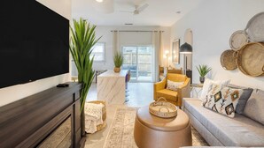 A modern living room with a flat-screen TV, a sofa, a coffee table, and a dining area with a marble island. - The Cannon Cottage by Avantstay Old Mt. Pleasant Gem Near Sullivans Island (Mount Pleasant)
