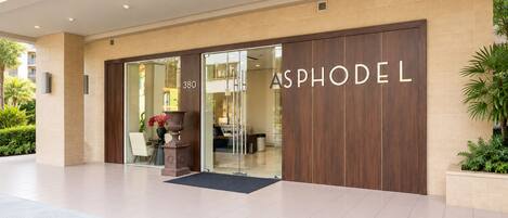 Entrada de un hotel con puerta de vidrio, fachada de madera y el nombre 'ASPHODEL' a la vista.