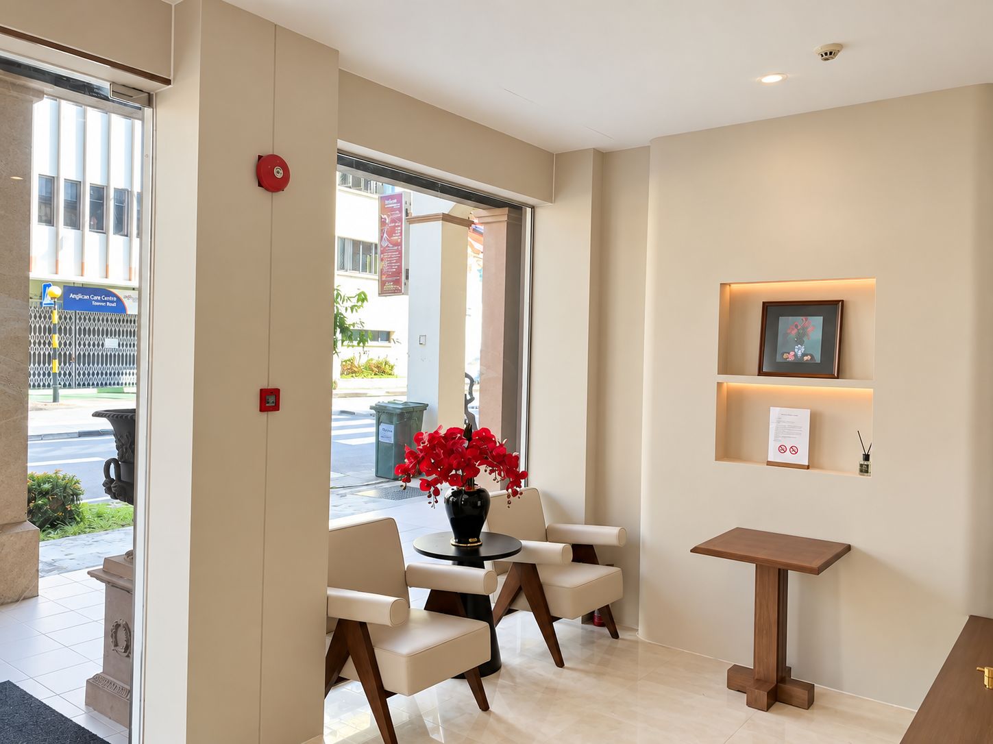 A hotel lobby with a reception desk, seating area, and a view of the street outside.