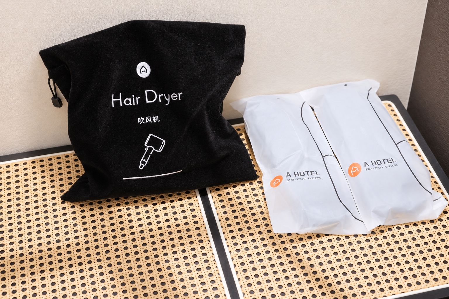 Una bolsa para secador de pelo negra y una bolsa de hotel blanca con la marca 'A HOTEL' sobre una bandeja perforada.