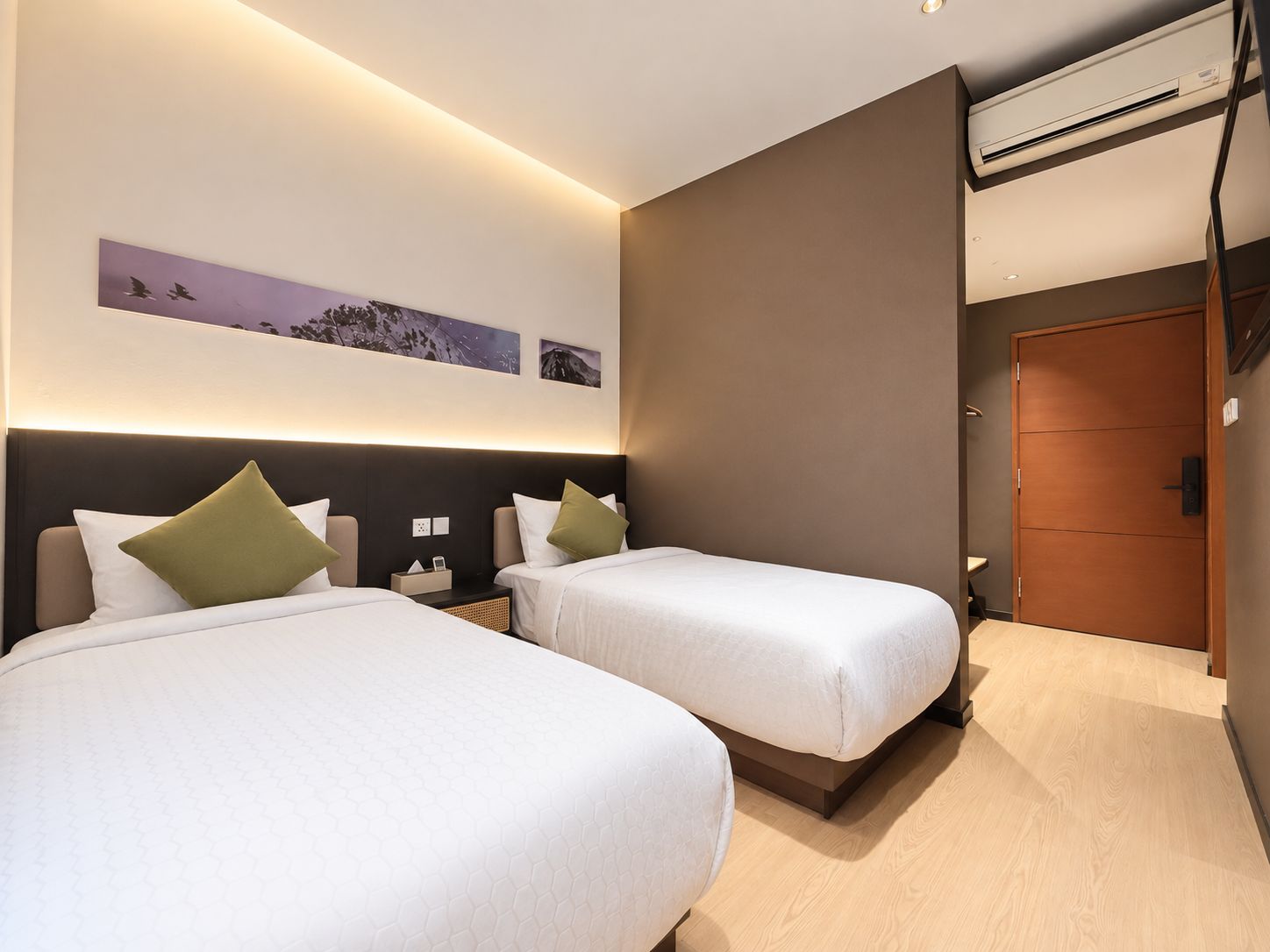 A hotel room with two beds, a wooden door, and a wall-mounted air conditioning unit.
