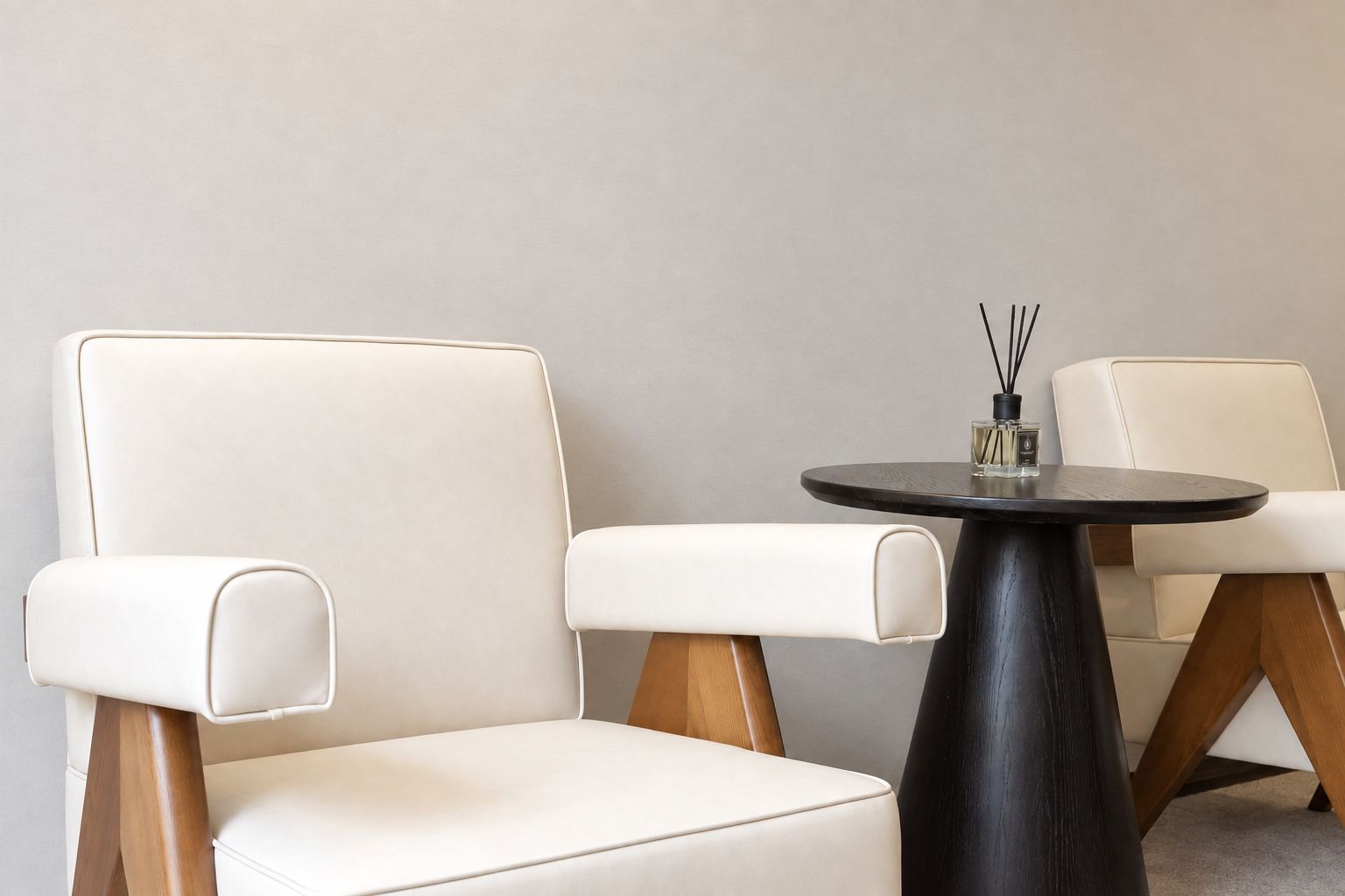 Quarto com duas poltronas de couro branco e uma mesa redonda preta com um frasco de perfume.