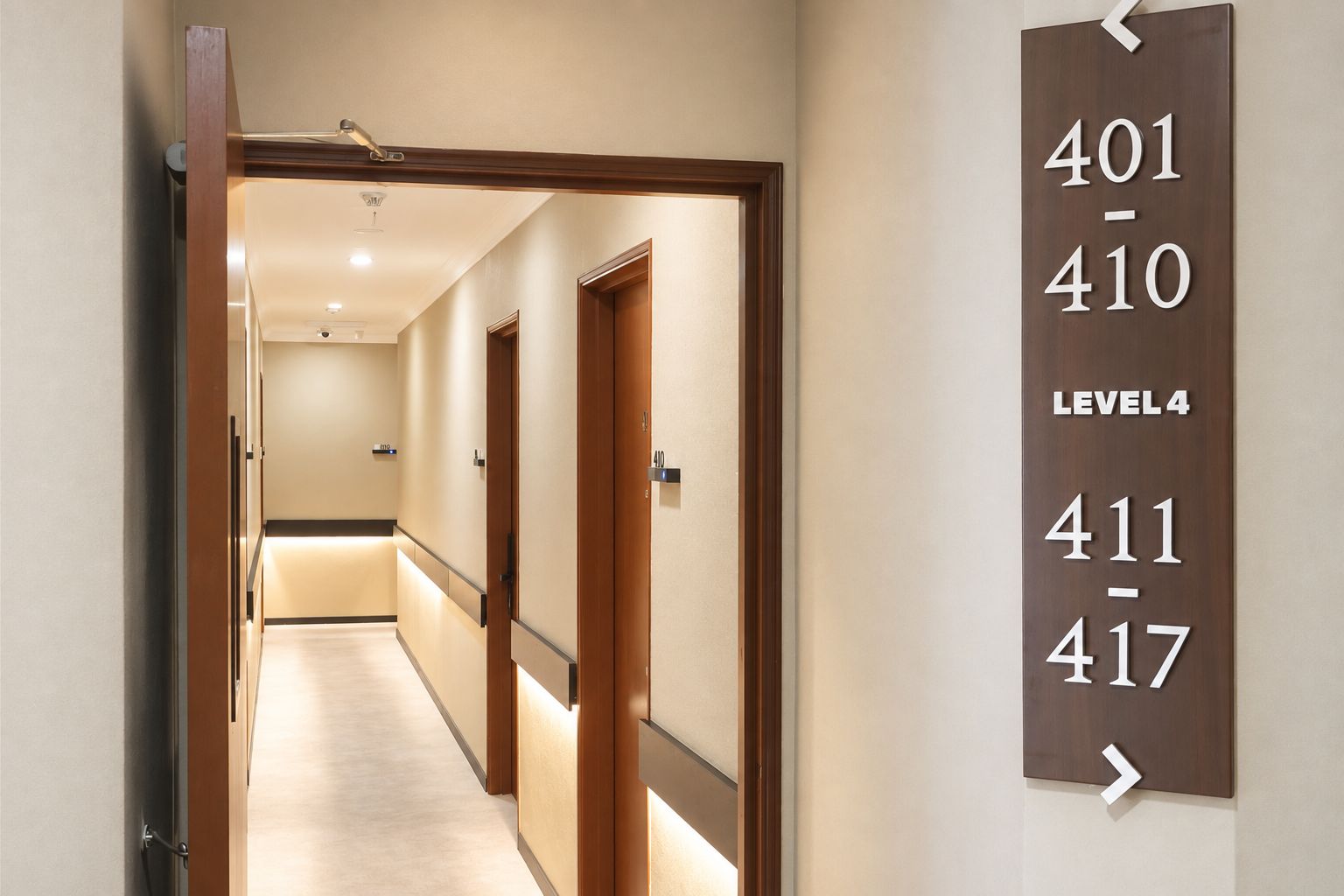 Ein Hotelkorridor mit Türen, die von 401 bis 417 nummeriert sind, was auf mehrere Zimmer hinweist. Der Korridor ist gut beleuchtet, mit einer Deckenleuchte, und der Boden ist mit Teppich ausgelegt. Ein Schild zeigt an, dass es sich um die vierte Etage handelt.