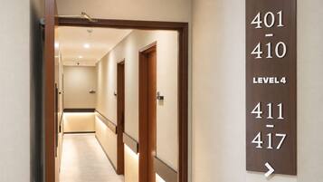 Ein Hotelkorridor mit Türen, die von 401 bis 417 nummeriert sind, was auf mehrere Zimmer hinweist. Der Korridor ist gut beleuchtet, mit einer Deckenleuchte, und der Boden ist mit Teppich ausgelegt. Ein Schild zeigt an, dass es sich um die vierte Etage handelt.