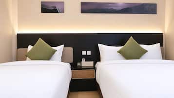 Habitación de hotel con dos camas, cada una con ropa blanca y almohadas verdes, una mesita de noche con una lámpara y dos cuadros en la pared.