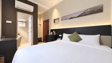 Habitación de hotel con una cama grande, una mesita de noche, un equipo de aire acondicionado, un cuadro en la pared y una puerta que da al baño.