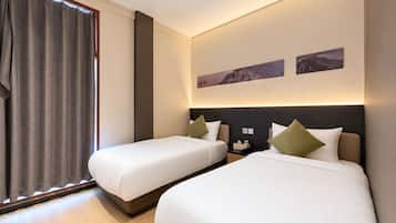 Quarto de hotel com duas camas, uma janela grande com cortinas, mesa de cabeceira e uma obra de arte na parede.