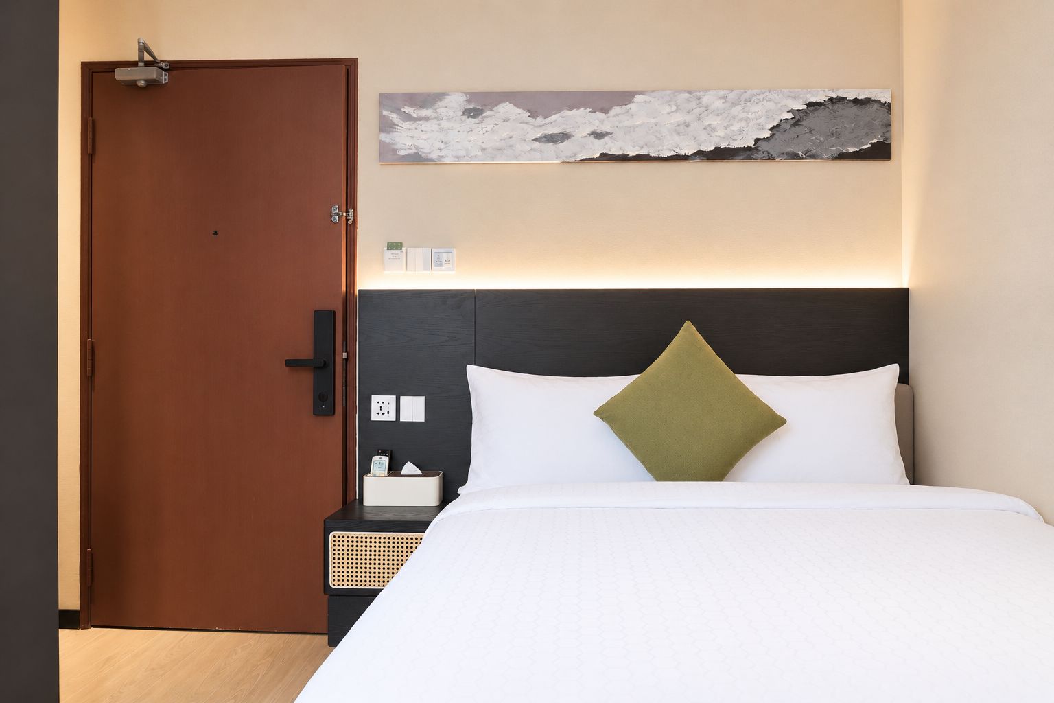 Una habitación de hotel con cama, mesita de noche, una obra de arte en la pared y una puerta.