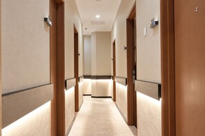 A hotel hallway with wooden doors, a carpeted floor, and a light-colored wall. - Asphodel Inn - Newly Renovated (Singapore)