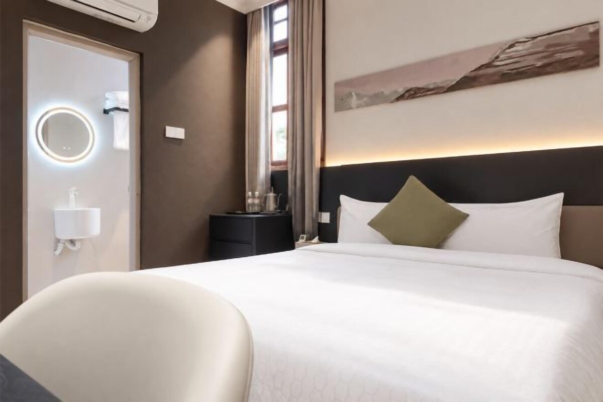 A hotel room with a bed, a bedside table, a mirror, and a window with curtains.