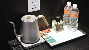 A coffee maker, two water bottles, a bottle of perfume, and a smartphone on a table. - Asphodel Inn - Newly Renovated (Singapore)