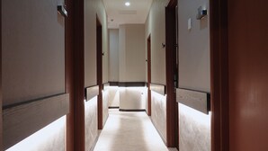 A hotel corridor with wooden doors, a carpeted floor, and a light-colored wall. - Asphodel Inn - Newly Renovated (Singapore)