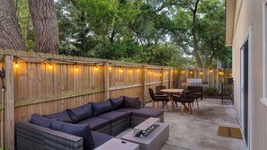 An outdoor patio with a wooden fence, string lights, a grill, a sofa, and a dining table. - Near Sullivans Island & Downtown w/ Outdoor Dining The Arsenal by Avantstay (Mount Pleasant)