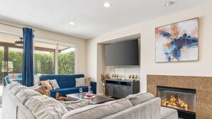 A modern living room with a grey sectional sofa, a blue sofa, a flat-screen TV, a fireplace, and a large abstract painting on the wall. - Casa Campo 5BR Desert Oasis w/ Pool, Firepit, & Outdoor Lounge (Indio)