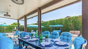 An outdoor dining area with a covered patio, blue upholstered chairs, and a table set for a meal. - Casa Campo 5BR Desert Oasis w/ Pool, Firepit, & Outdoor Lounge (Indio)