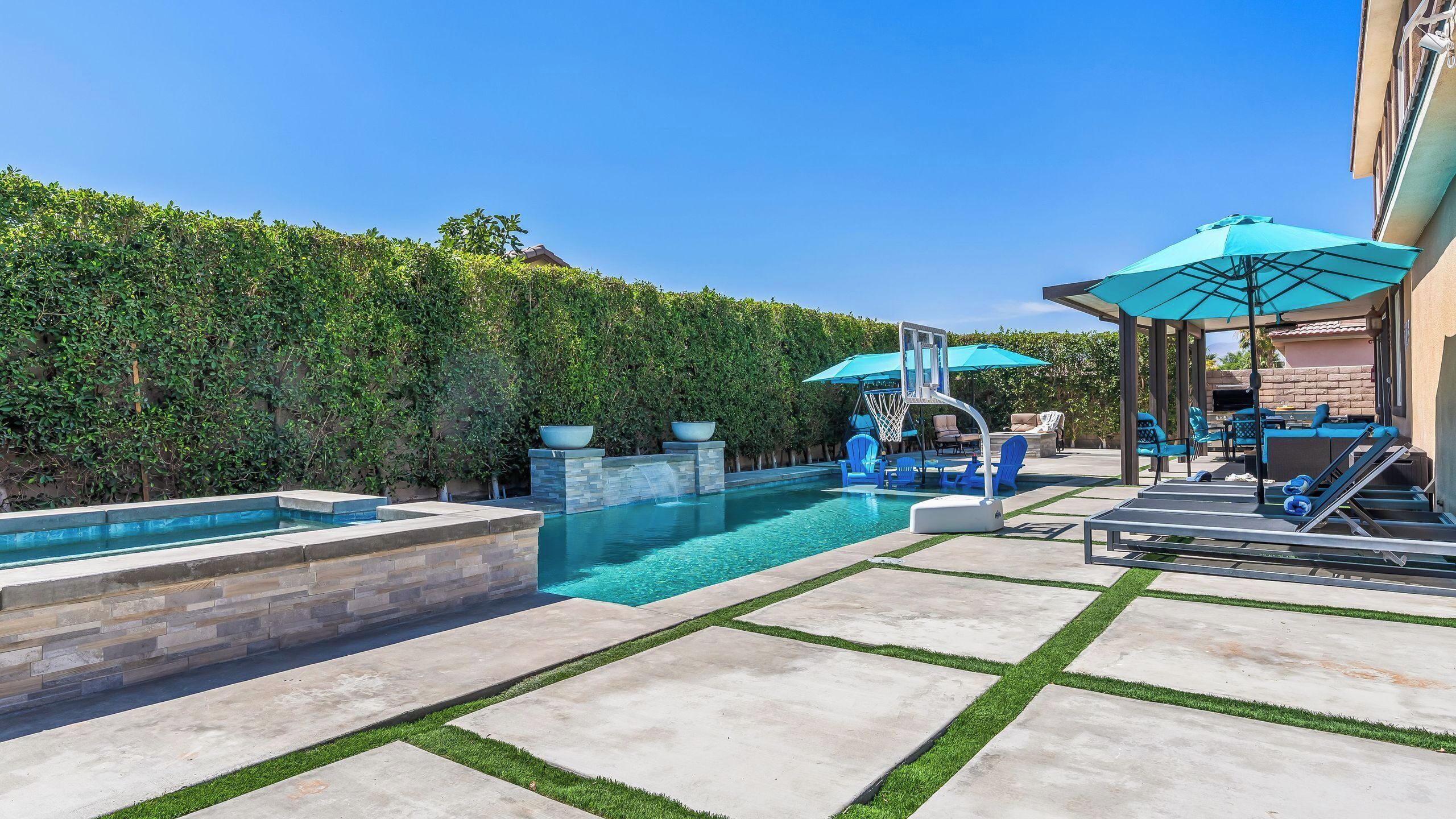 Un jardin avec une piscine, un panier de basketball et un espace salon extérieur.