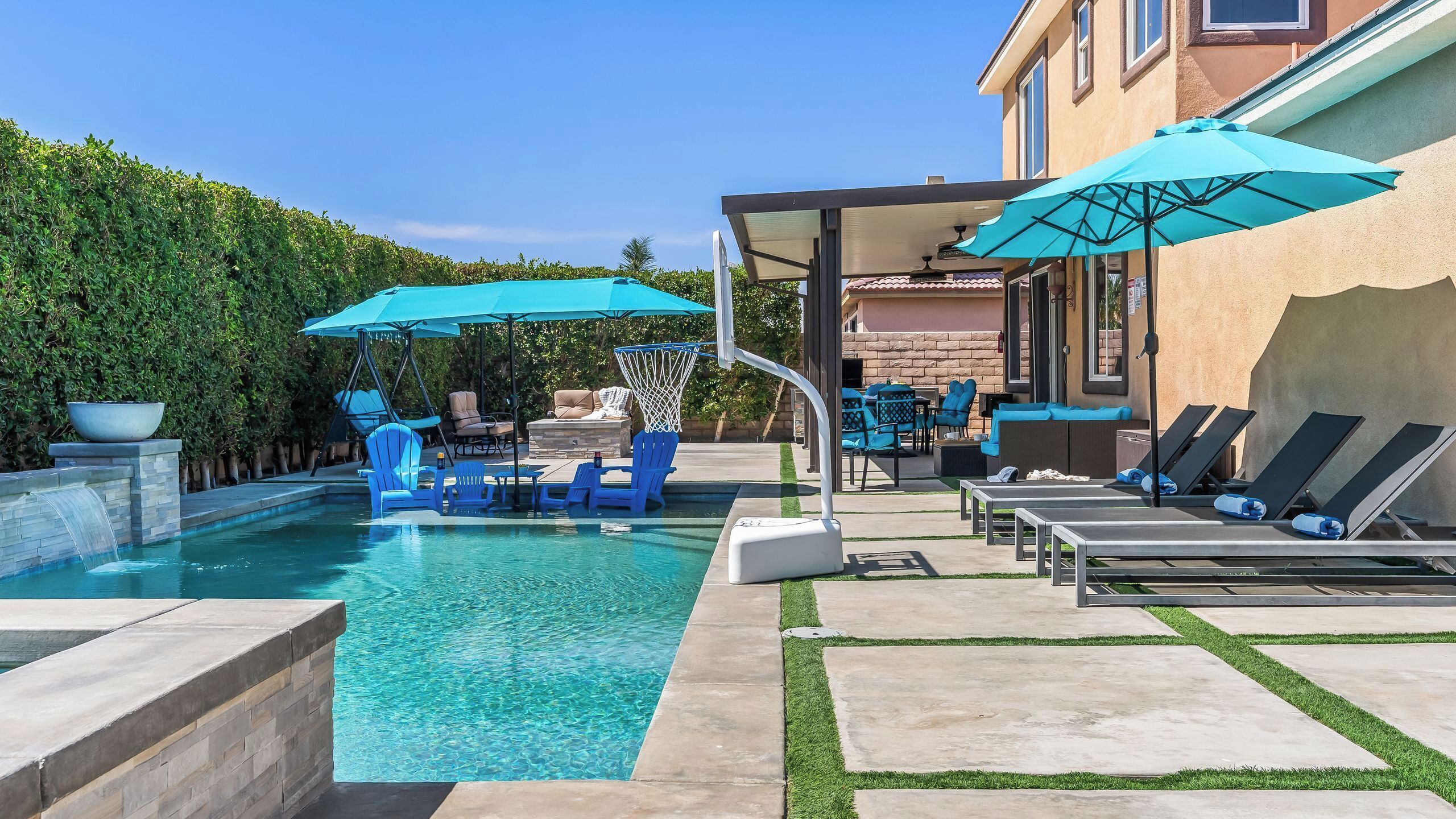 A swimming pool with blue chairs and umbrellas, a covered seating area, and a stone wall.