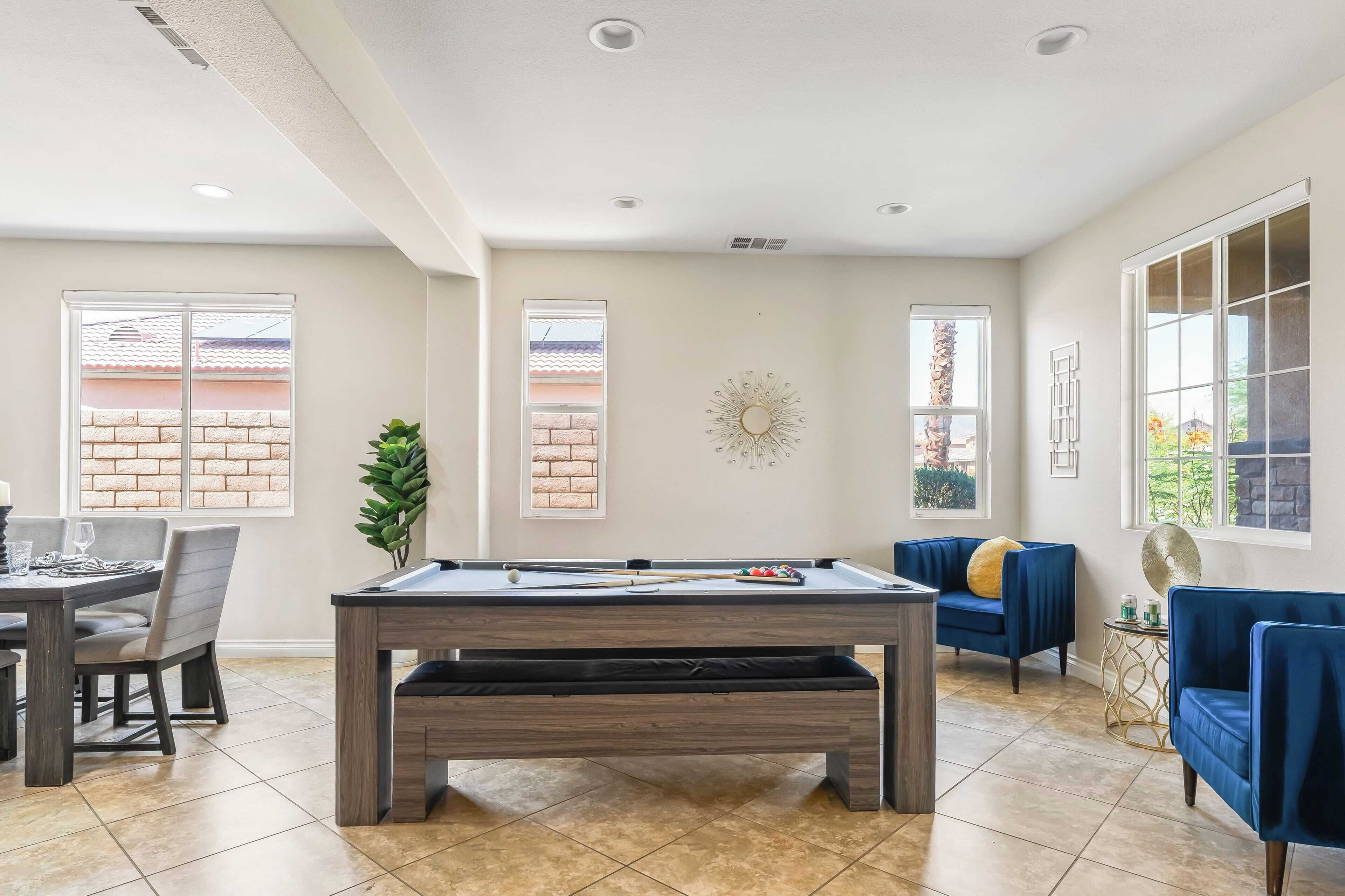 A spacious living area with a pool table, comfortable seating, and large windows offering views of the outside.