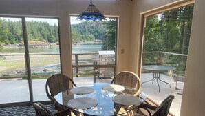 Comedor con una mesa redonda de vidrio y sillas de mimbre, con vistas a un lago y un bosque.