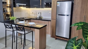 A modern kitchen with dark cabinets, a stainless steel refrigerator, a central island with bar stools, and a tiled backsplash.