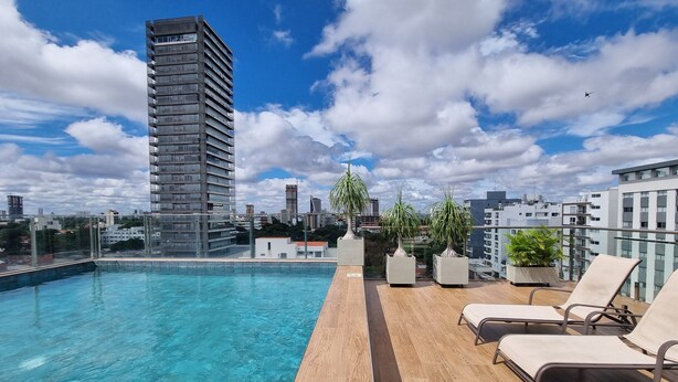 A rooftop pool with clear blue water, surrounded by lounge chairs and potted plants.