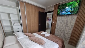 A neatly arranged bedroom with a bed, a wardrobe, a television, and a mirror.