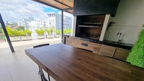 A modern kitchen with a dark wooden table and cabinets, a built-in oven, and a view of the cityscape through large windows.