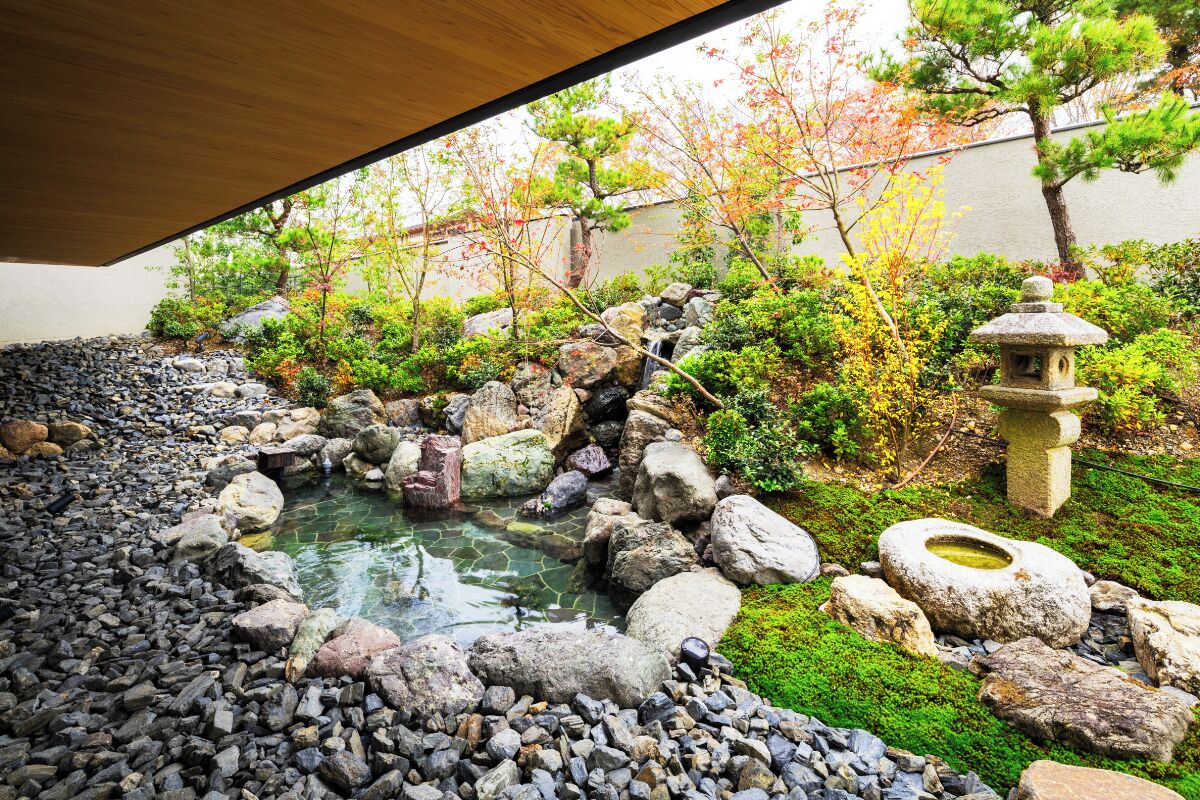 Un jardin japonais traditionnel avec un étang, des rochers et une lanterne en pierre.