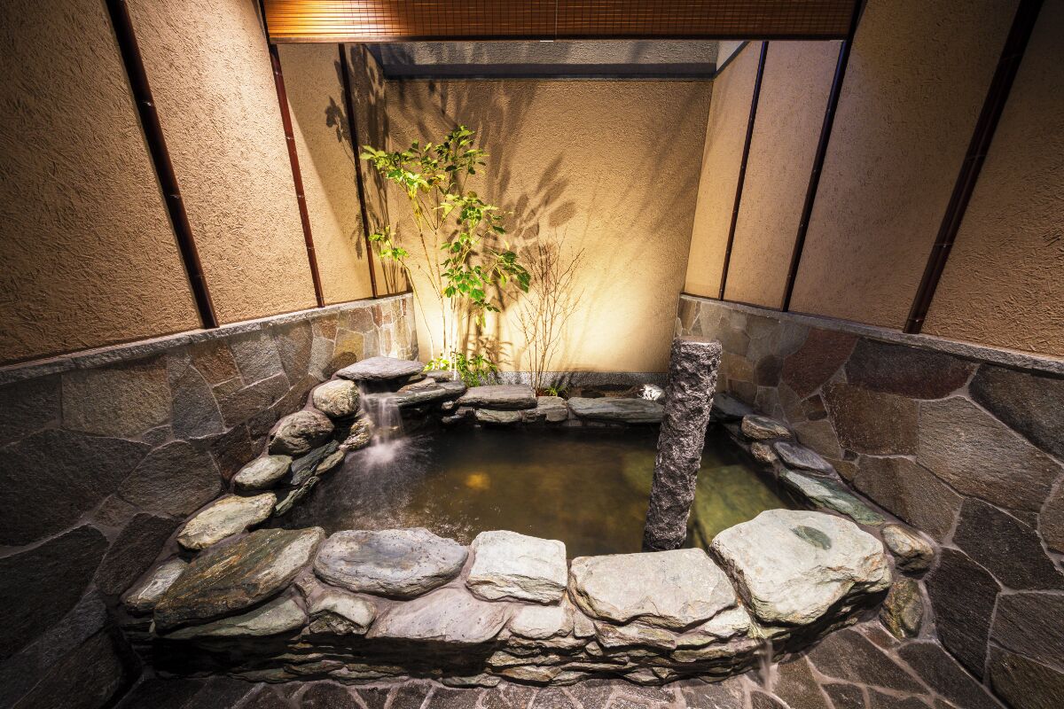 A stone-walled hot spring area with a small waterfall and a plant.