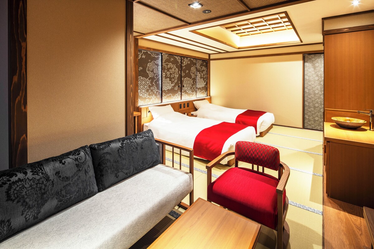 A hotel room with a sofa, two beds, a wooden cabinet, and a traditional Japanese sliding door.
