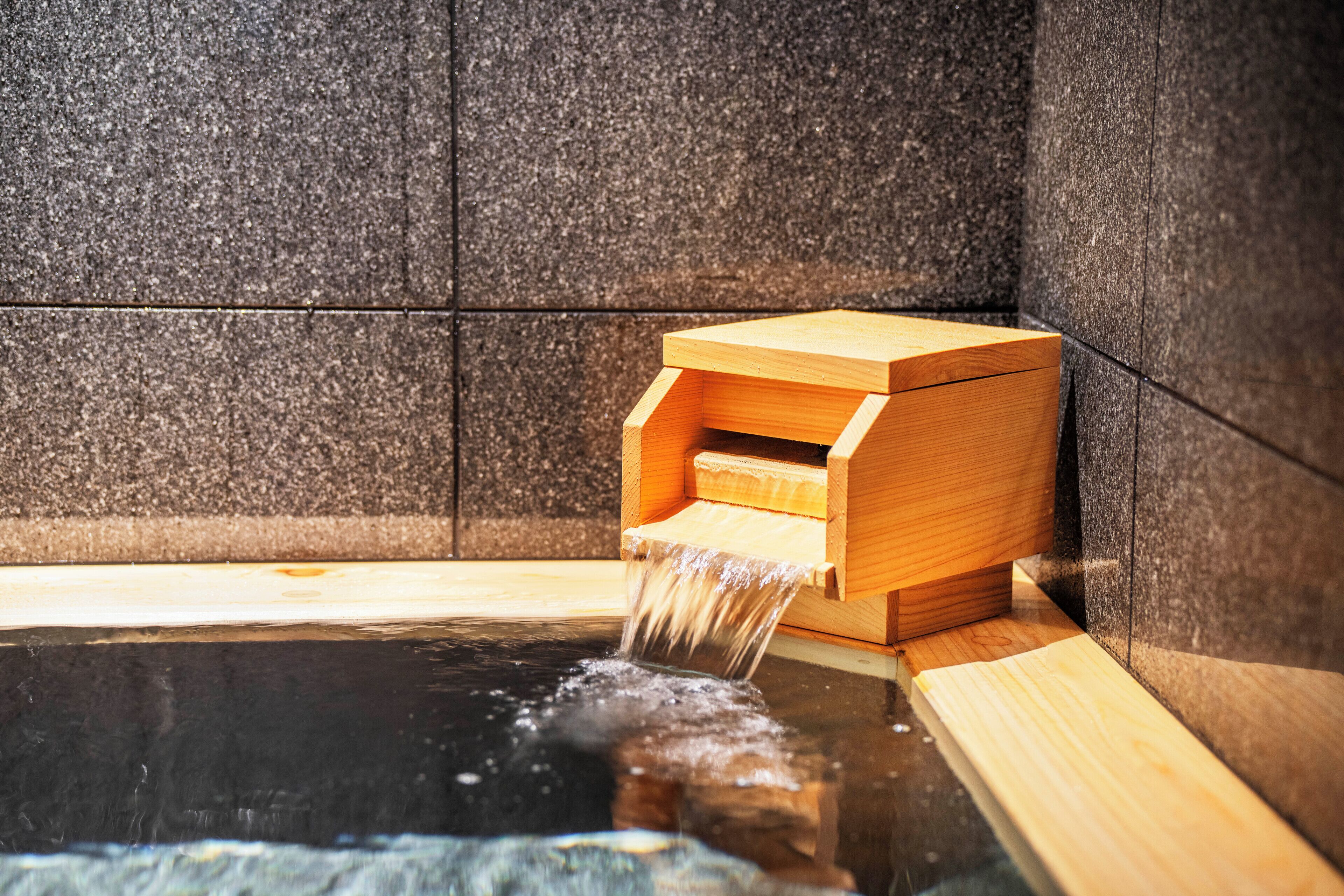 A wooden water feature with a wooden box structure, a black tiled wall, and a reflective water surface.