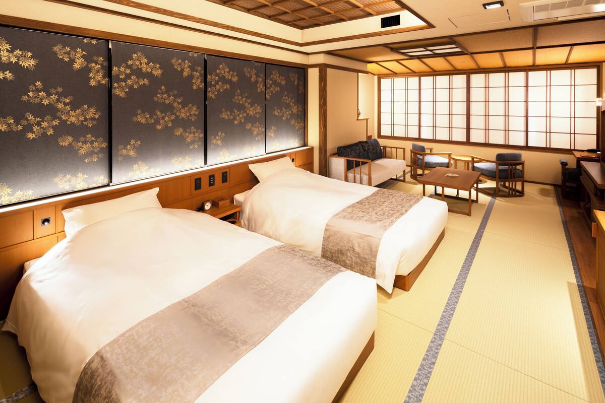 Habitación de hotel tradicional japonesa con dos camas, suelo de tatami, puertas correderas shoji y vistas a la ciudad.