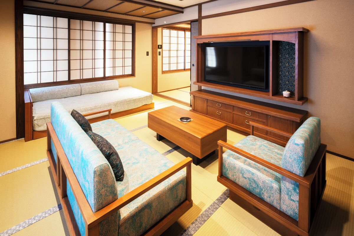 A traditional Japanese-style room with tatami flooring, a low wooden table, a sofa, and a television set.