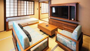 A traditional Japanese-style room with tatami flooring, a low wooden table, a sofa, and a television set.