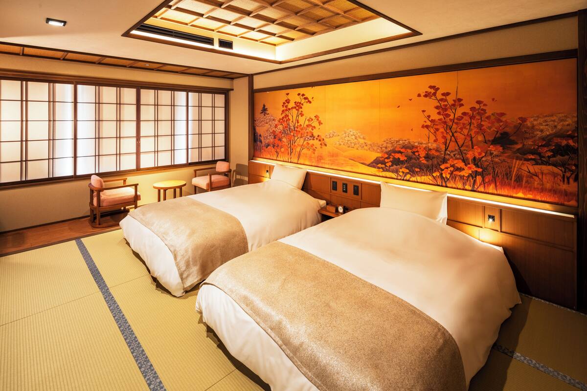 Habitación de hotel con dos camas, esteras de tatami, una pintura tradicional japonesa y una puerta corredera.