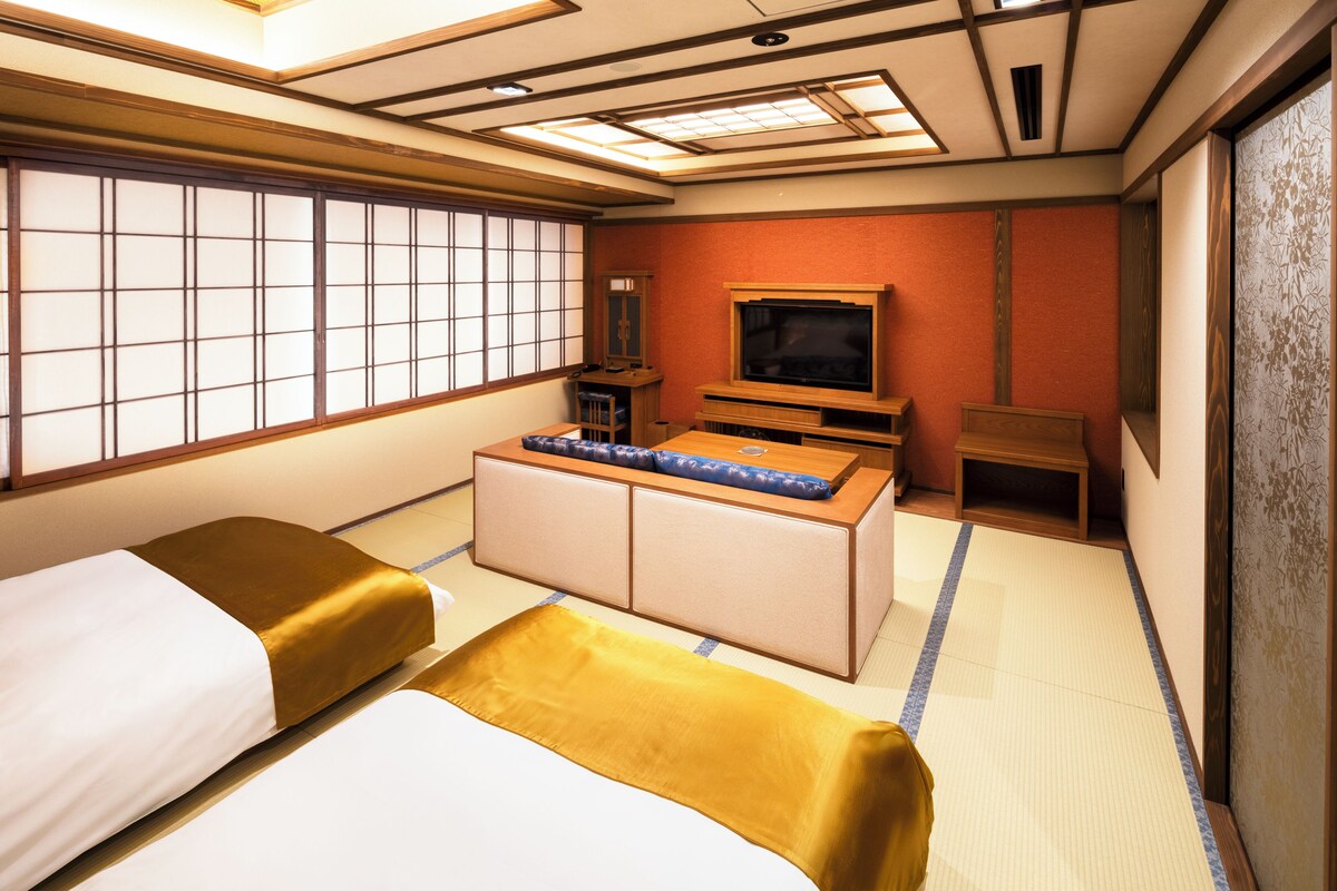 A traditional Japanese room with tatami flooring, a low wooden bed, a television, and a small table.