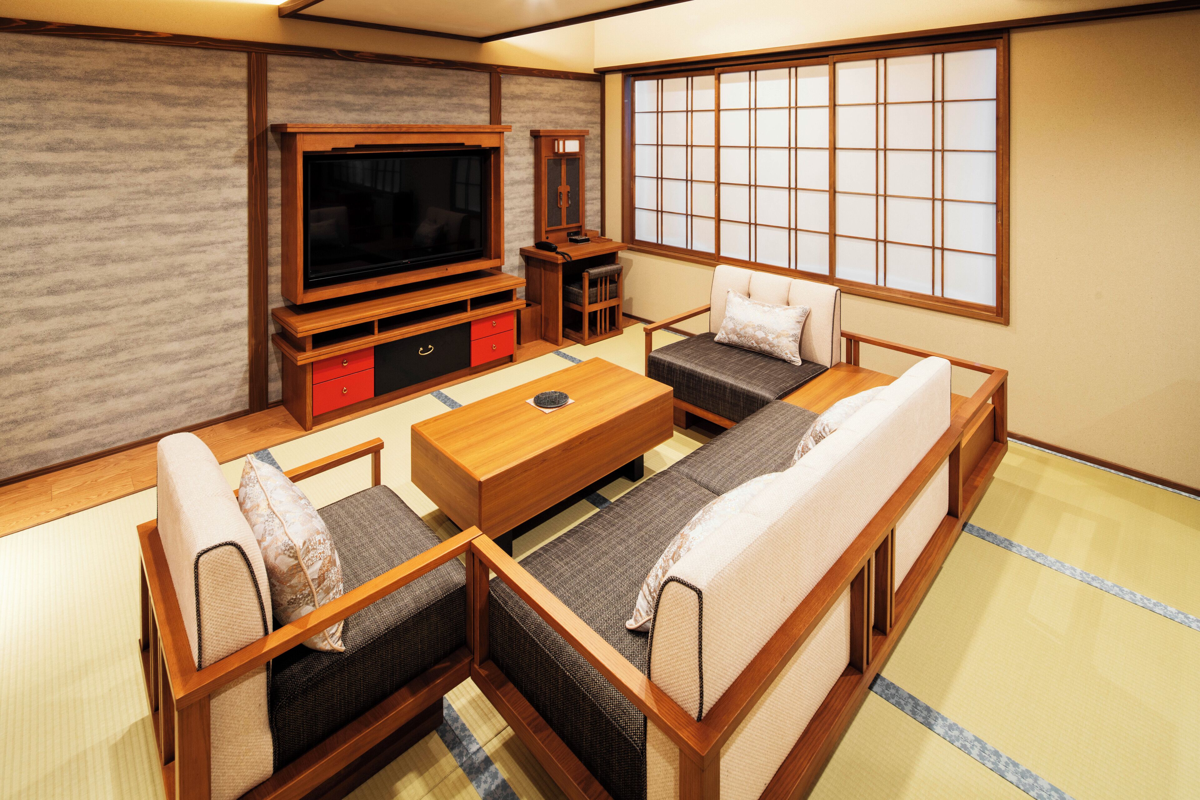 Un tradizionale soggiorno in stile giapponese con pavimento in tatami, un tavolino in legno basso, un divano, una televisione e una porta scorrevole con motivo a griglia.