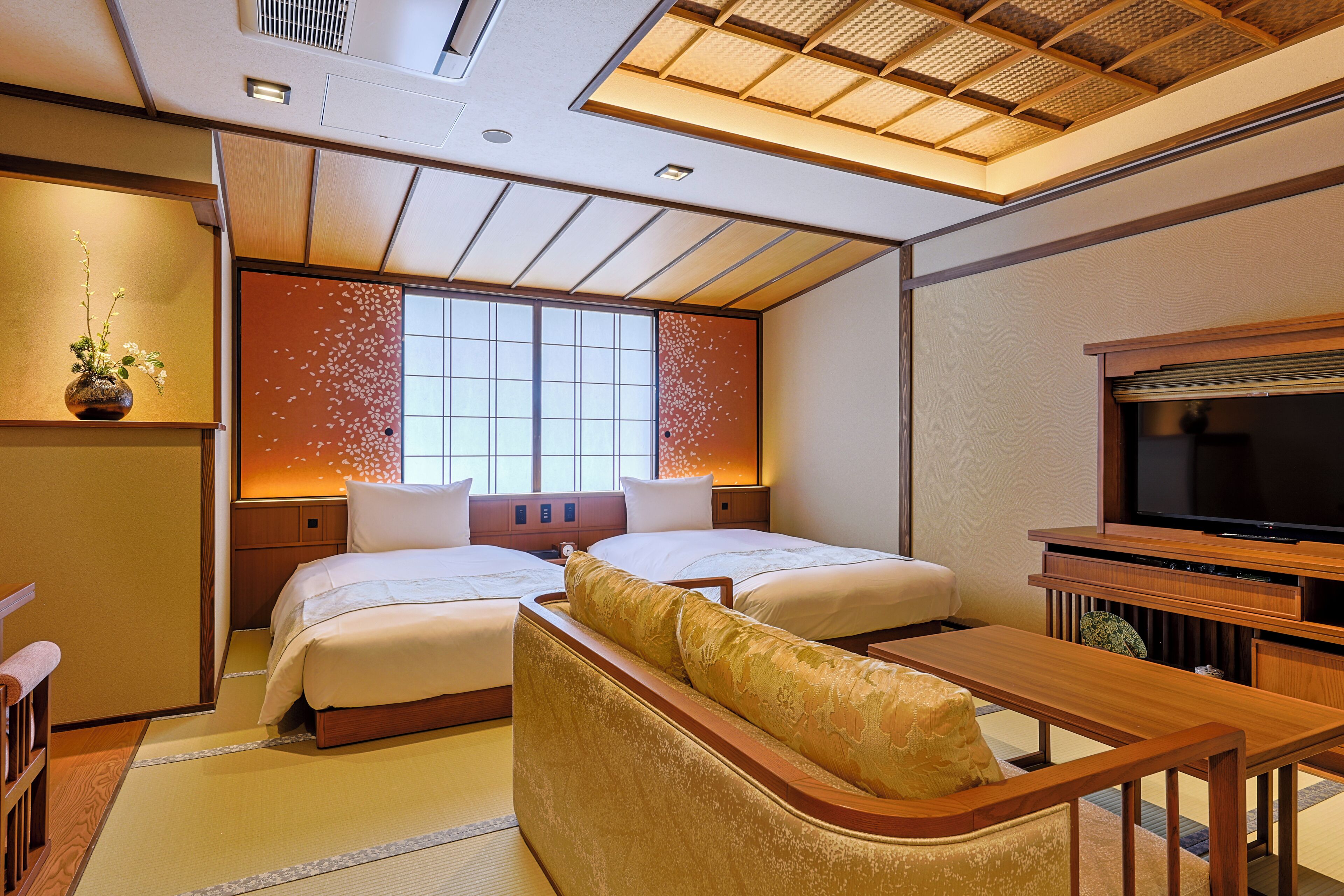 Habitación de hotel con una cama grande, un televisor, un escritorio de madera y un sofá de estilo japonés tradicional.