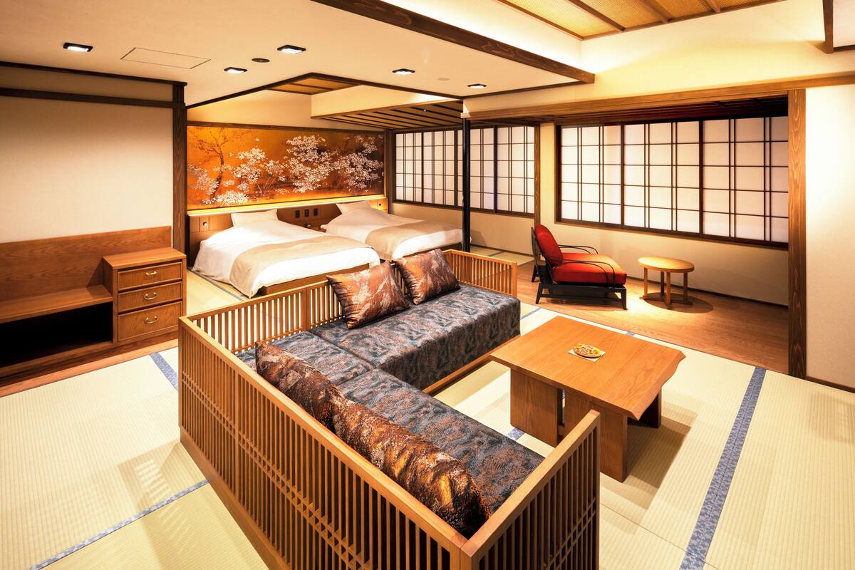 Una habitación tradicional japonesa con suelo de tatami, una cama baja de madera, un sofá, una pequeña mesa y una silla roja.