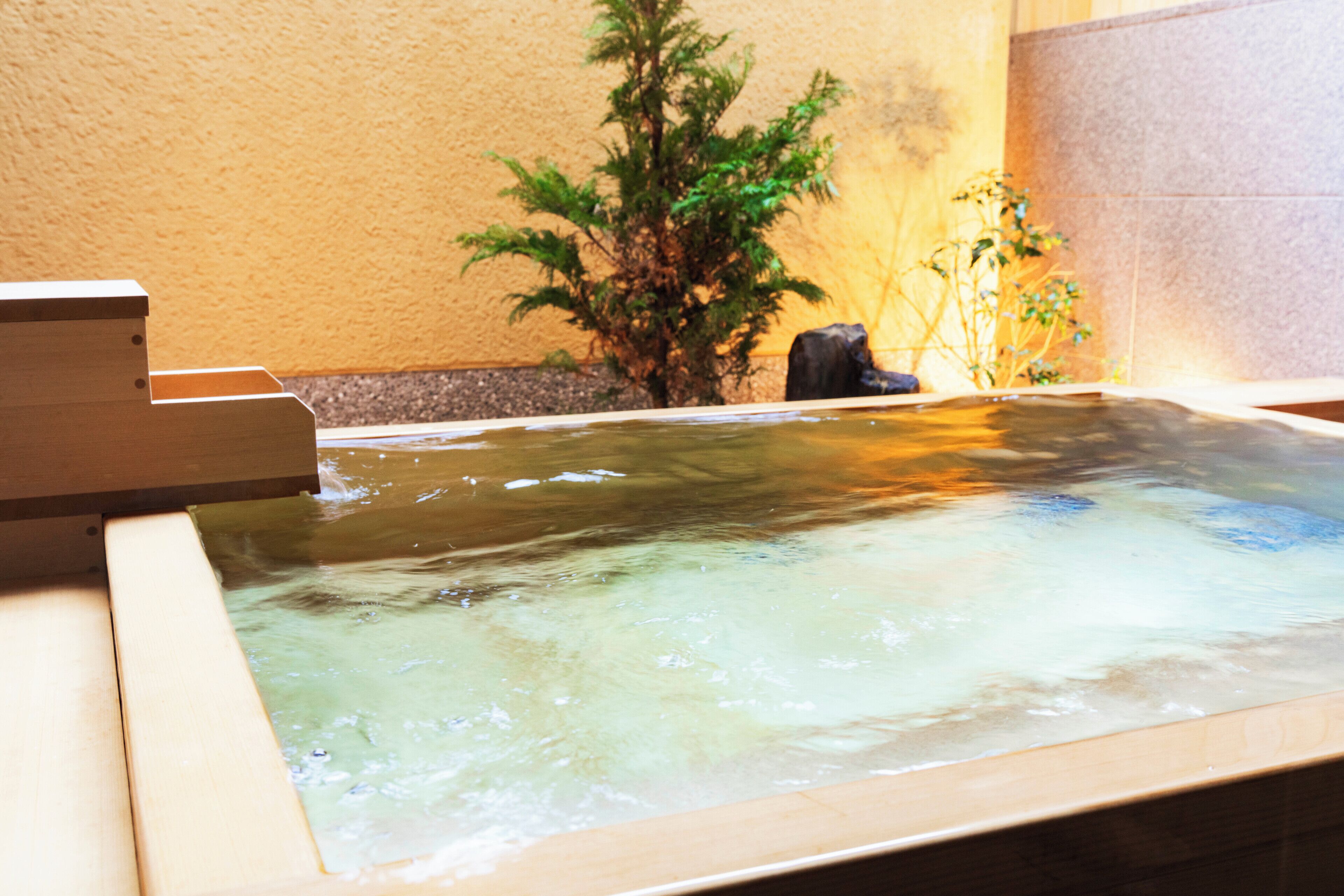 Un jacuzzi con un banco de madera, rodeado de plantas y un muro de piedra.