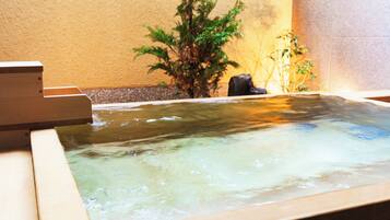 Un jacuzzi con un banco de madera, rodeado de plantas y un muro de piedra.