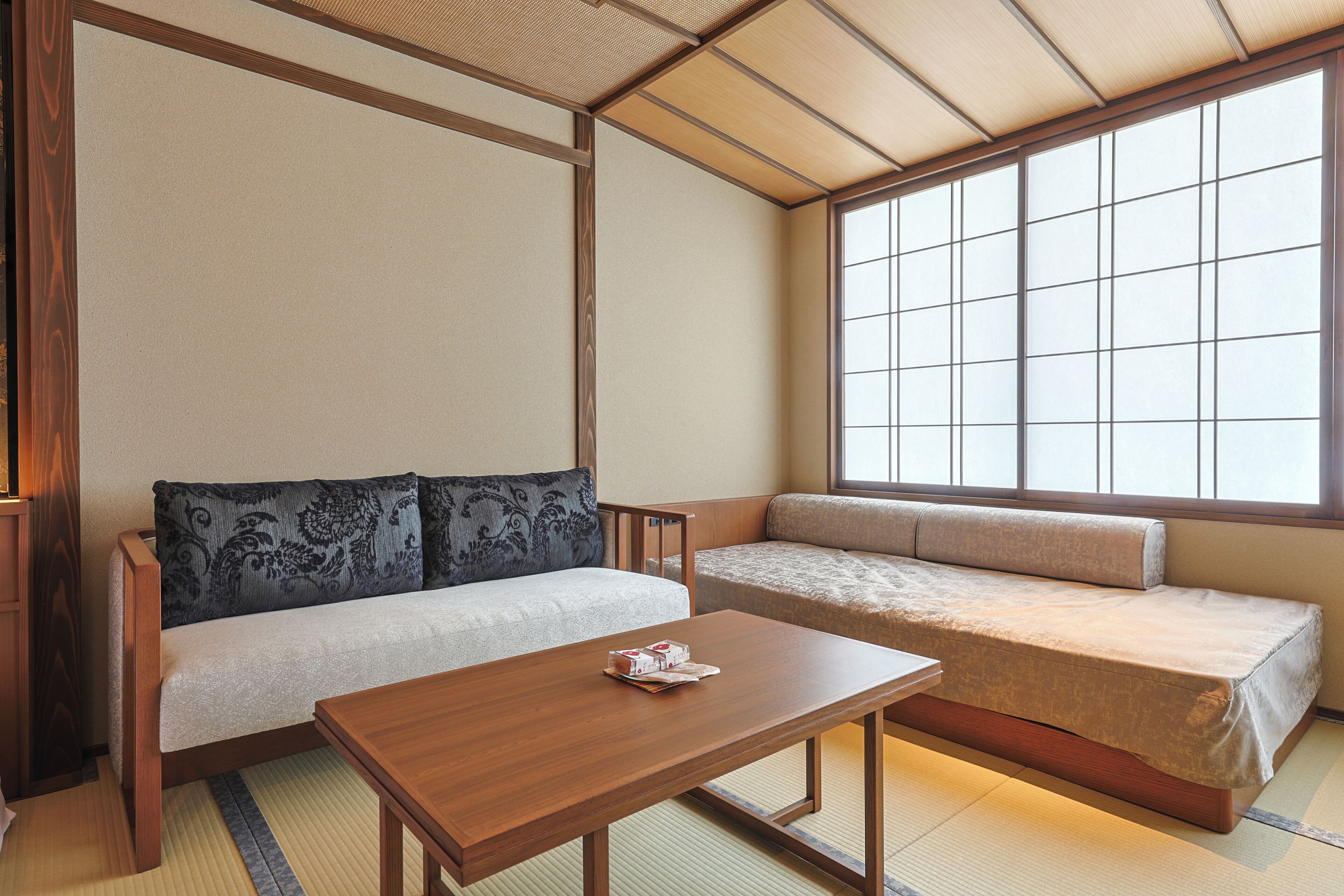 A traditional Japanese room with tatami flooring, a low wooden table, two tatami mats with cushions, and a large window.