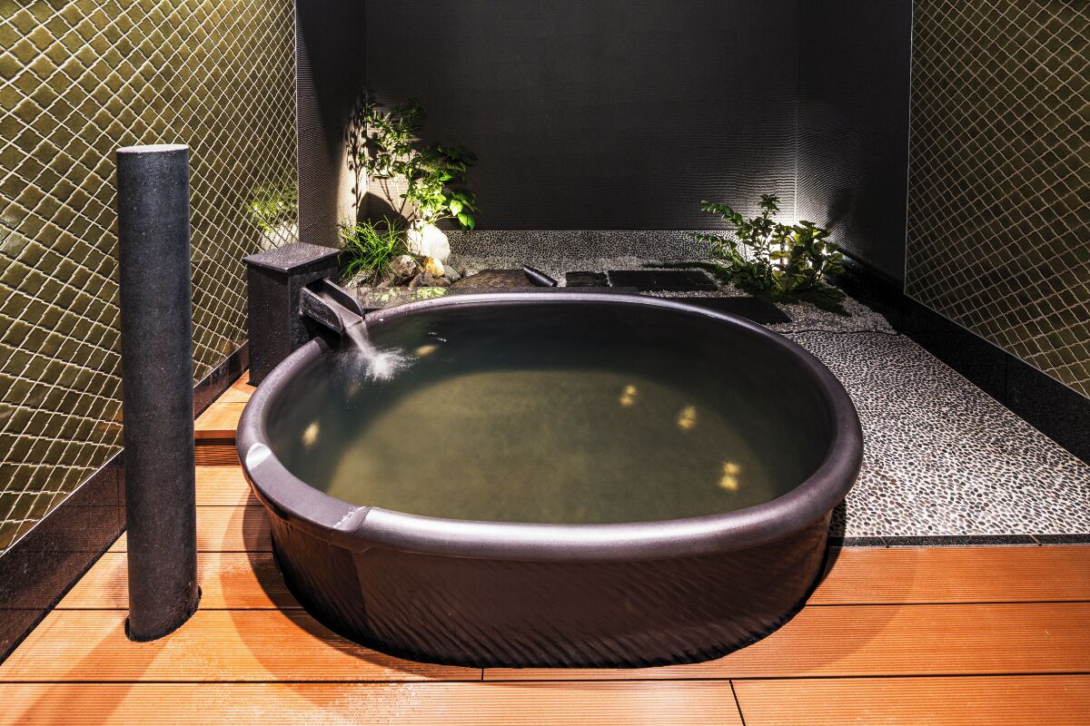 A hot tub with a wooden deck, surrounded by a tiled wall and a small plant.
