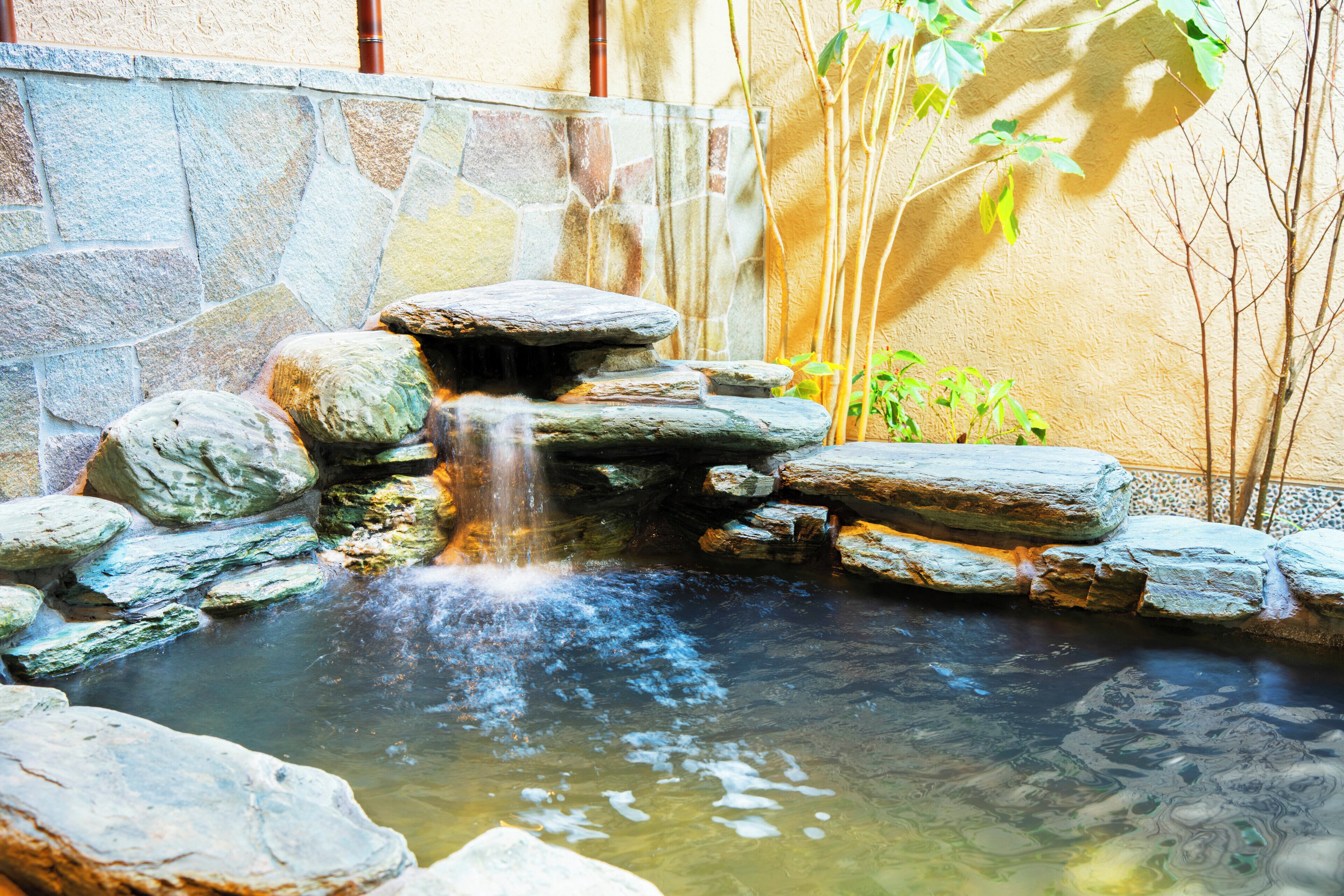 A stone waterfall in a garden with a stone wall and plants.